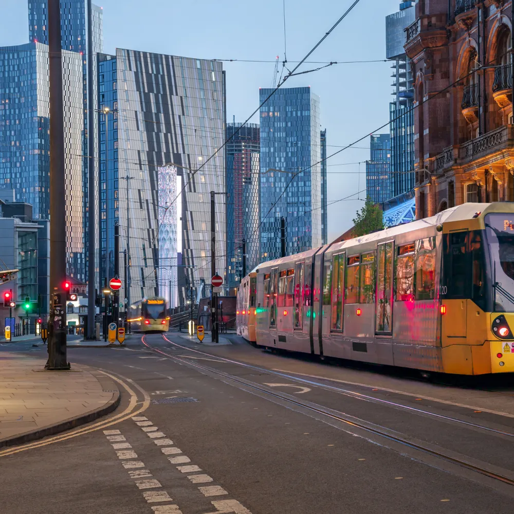 Manchester Metrolink tram passing city-centre offices at dusk