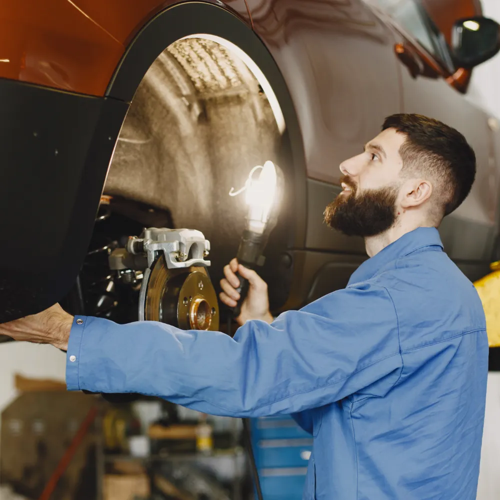 Mechanic in blue overalls inspecting a wheel arch on a lifted car