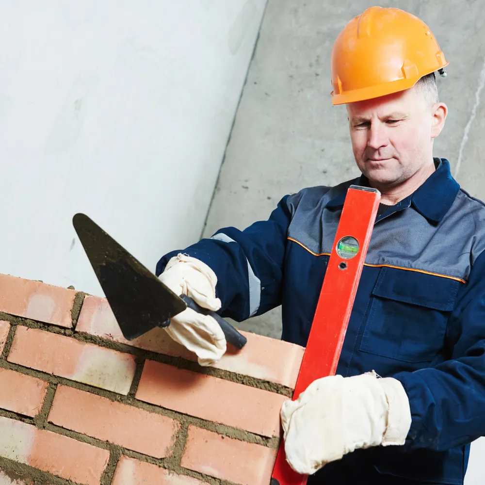 Bricklayer in gloves and a safety helmet laying bricks with a trowel and level