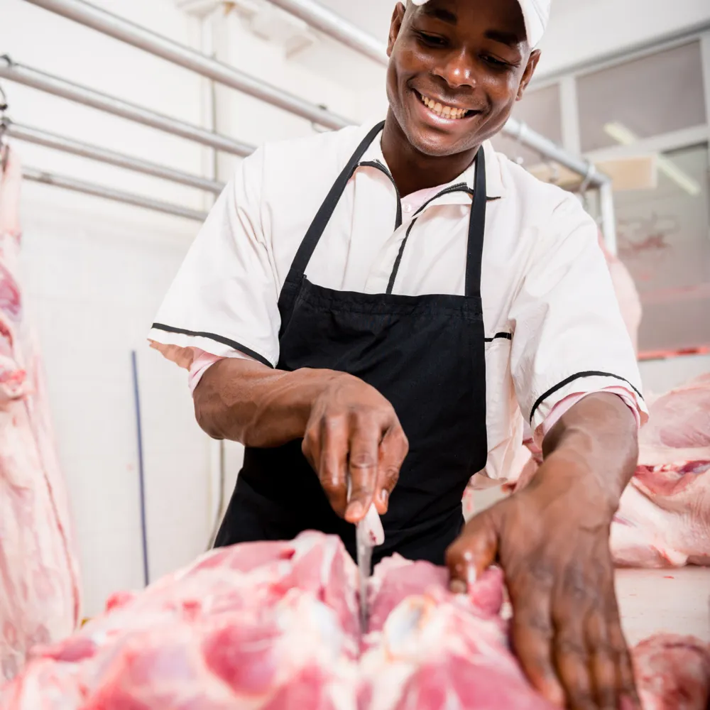 Butcher in an apron and cap breaking down meat at a cutting table