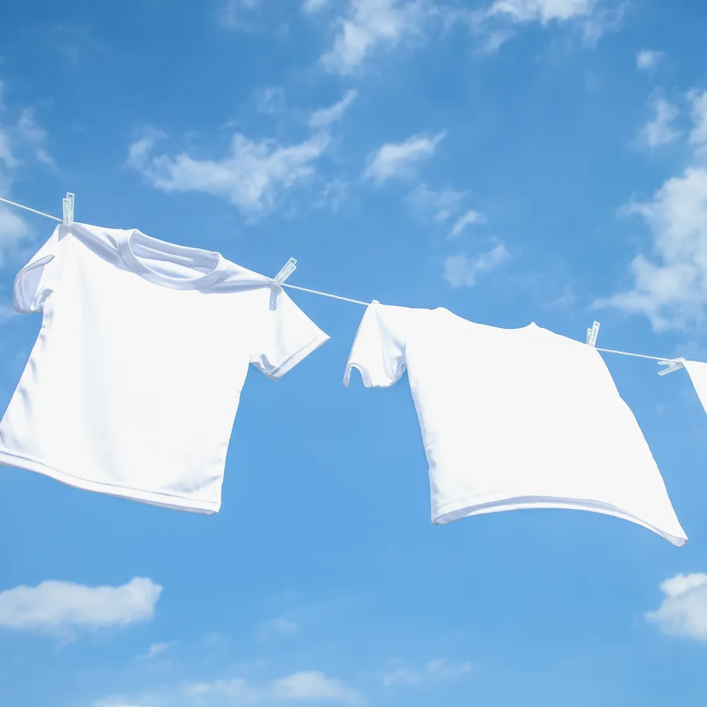 White tee shirts drying on a washing line against a blue sky