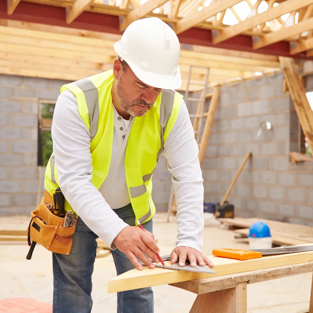 Carpenter in a hi-vis vest and tool belt marking a timber cut with a square