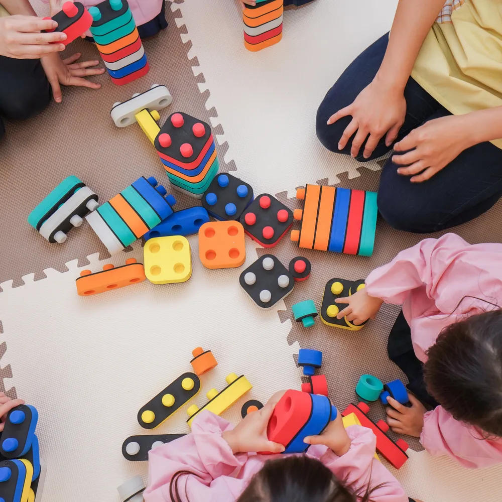 Nursery staff and children playing with building blocks on a soft play mat