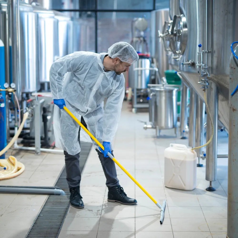 Industrial cleaning operative in protective coat and hairnet squeegeeing a plant floor