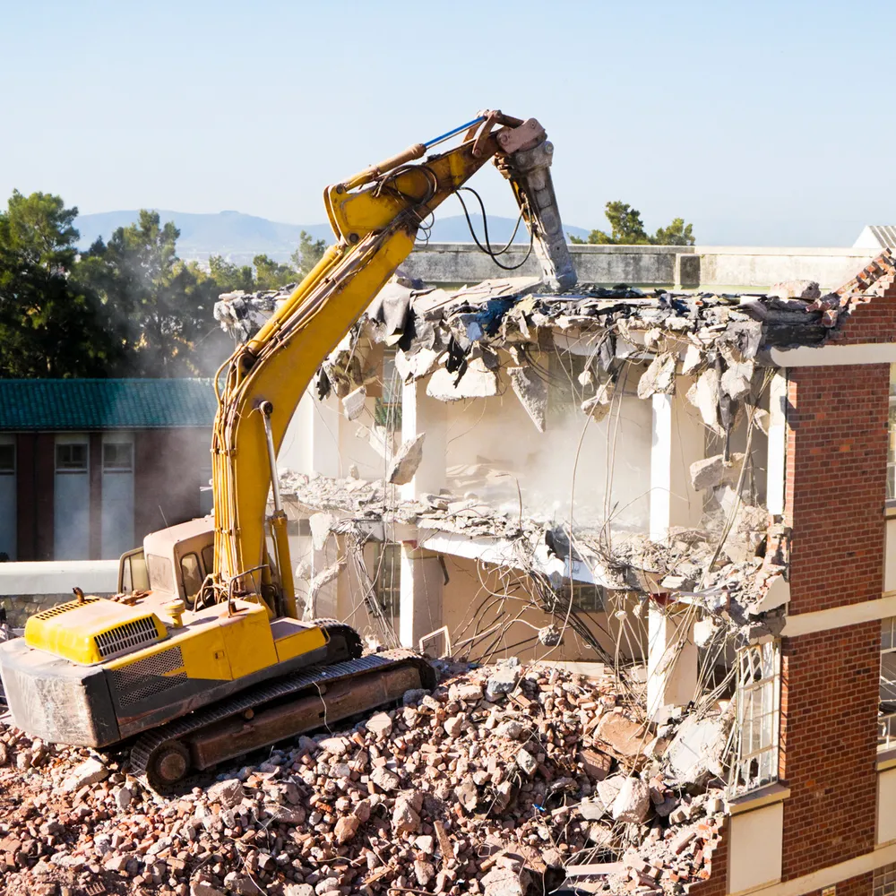 Excavator with breaker attachment demolishing a brick building