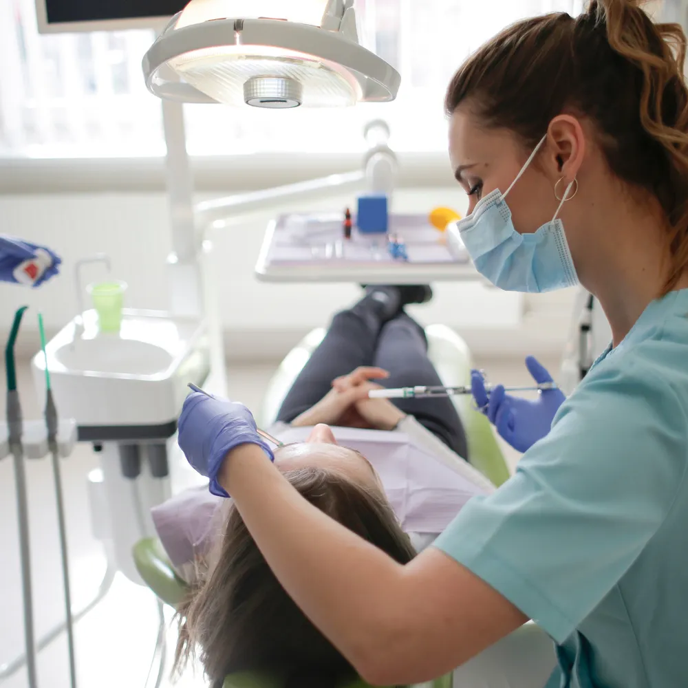 Dental nurse in scrubs, mask and gloves treating a patient