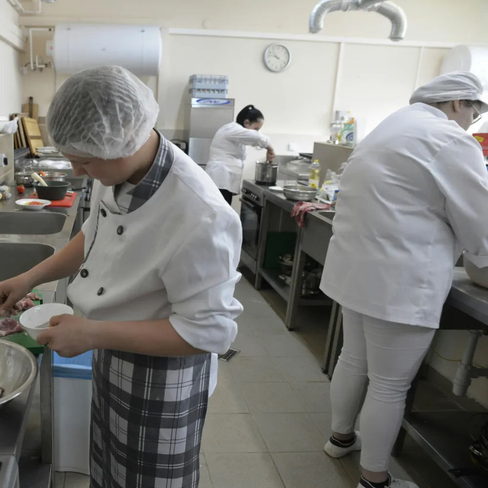 School catering staff in whites, aprons and hairnets working in a commercial kitchen