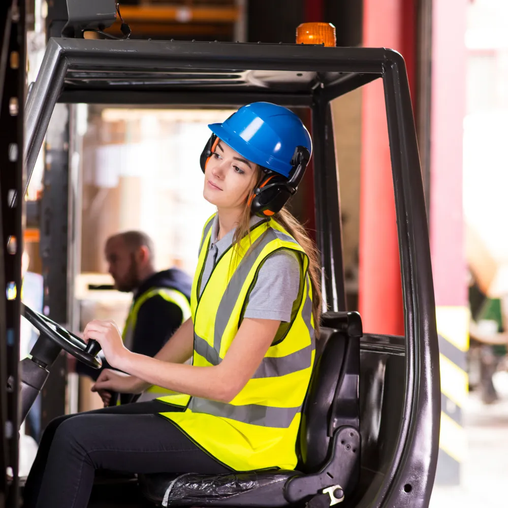 Forklift driver in a hi-vis vest, safety helmet and ear defenders at the wheel of a forklift