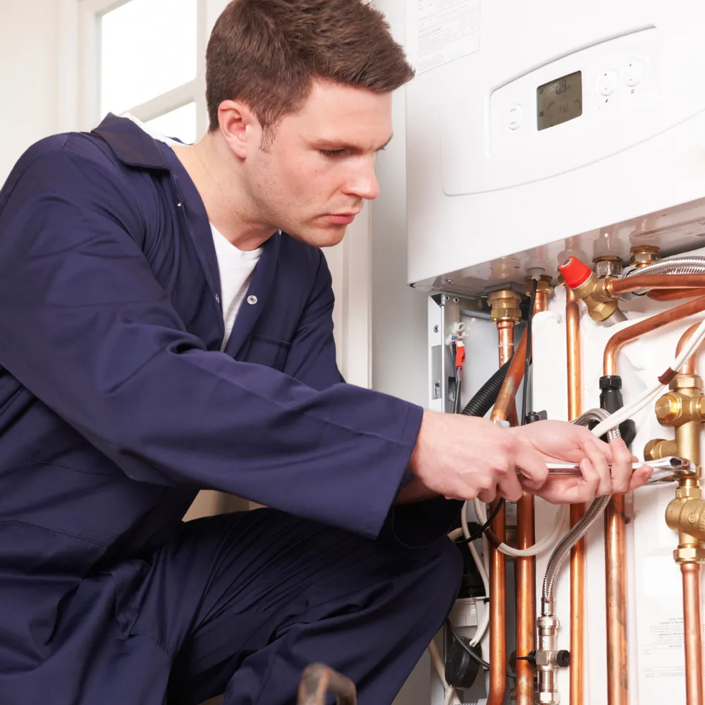 Gas engineer in navy coveralls servicing a wall-mounted boiler
