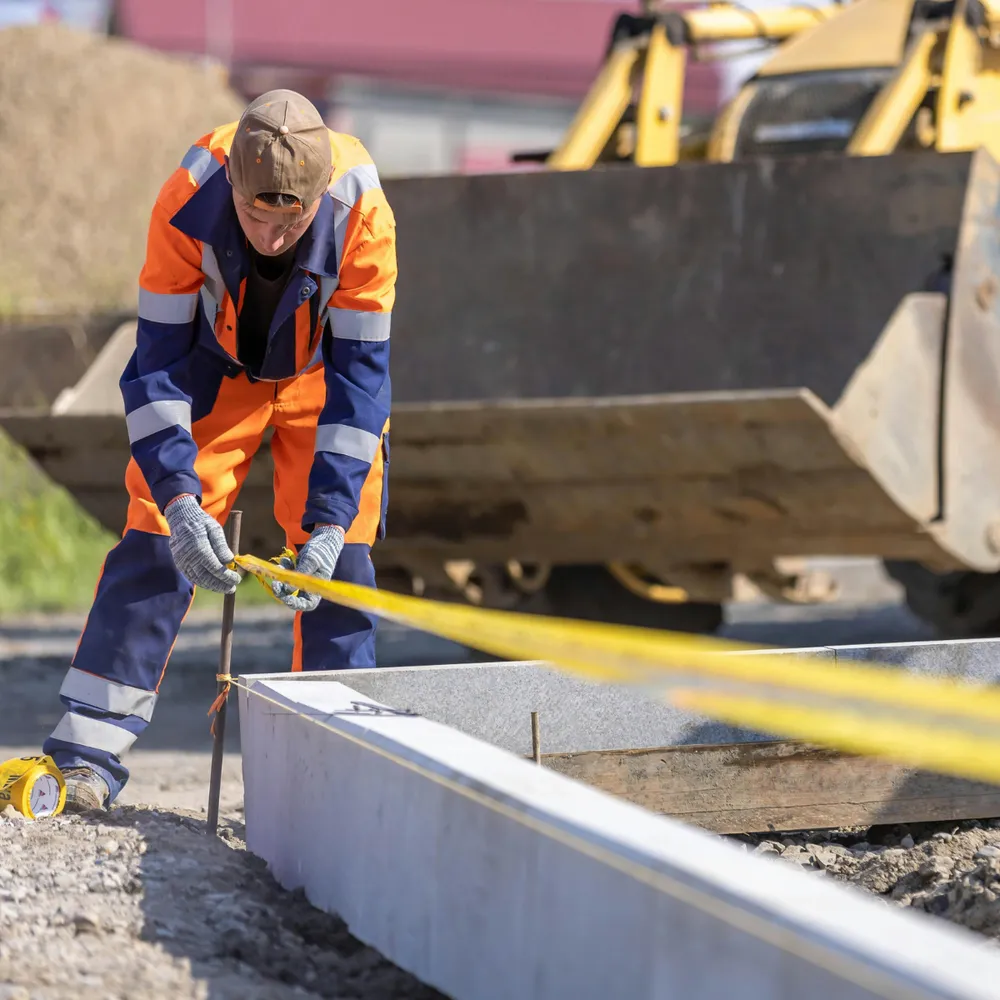 Groundworker in hi-vis setting out a concrete edge beam in front of an excavator