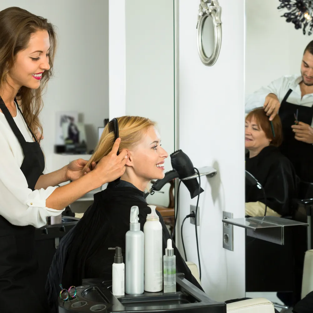 Hairdresser in a salon apron styling a client’s hair