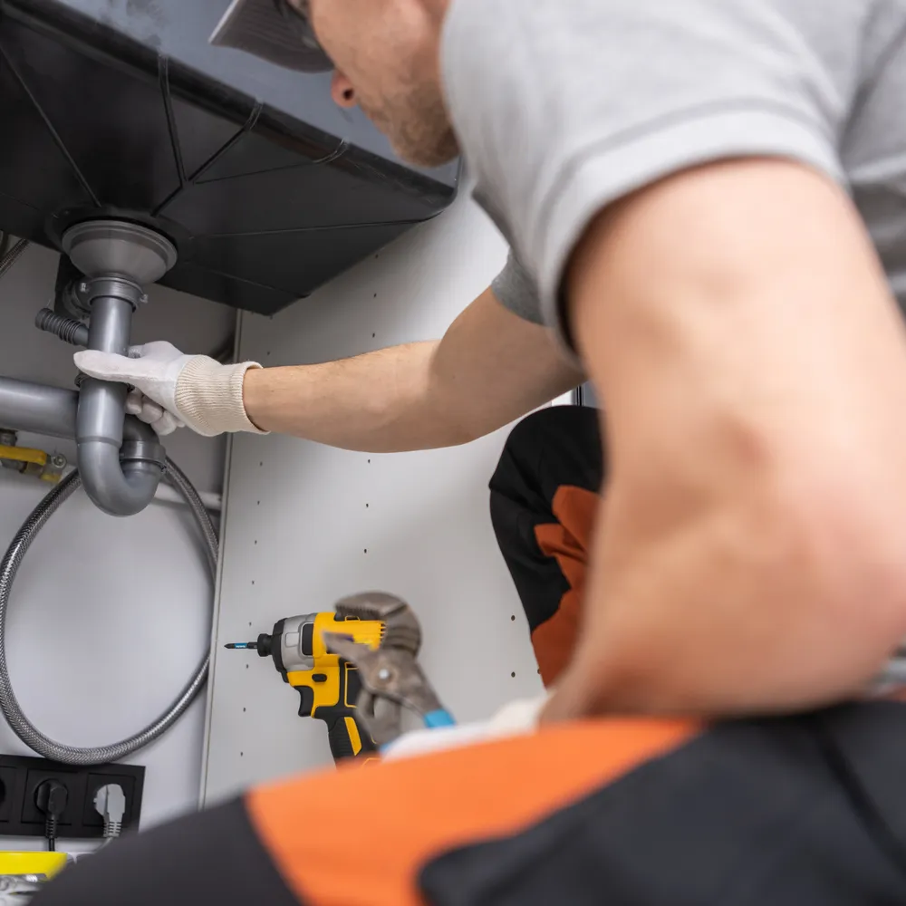 Maintenance engineer in work gloves repairing pipework under a sink