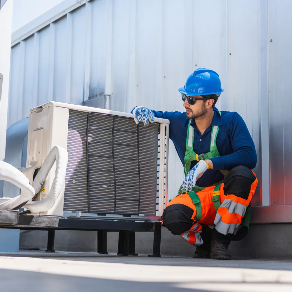 HVAC engineer in hi-vis trousers and safety helmet servicing a rooftop air-conditioning unit