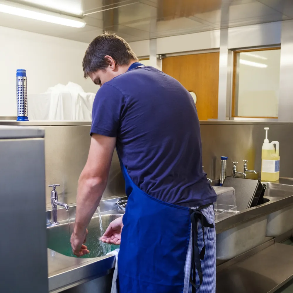 Kitchen porter in an apron washing up at a commercial kitchen sink