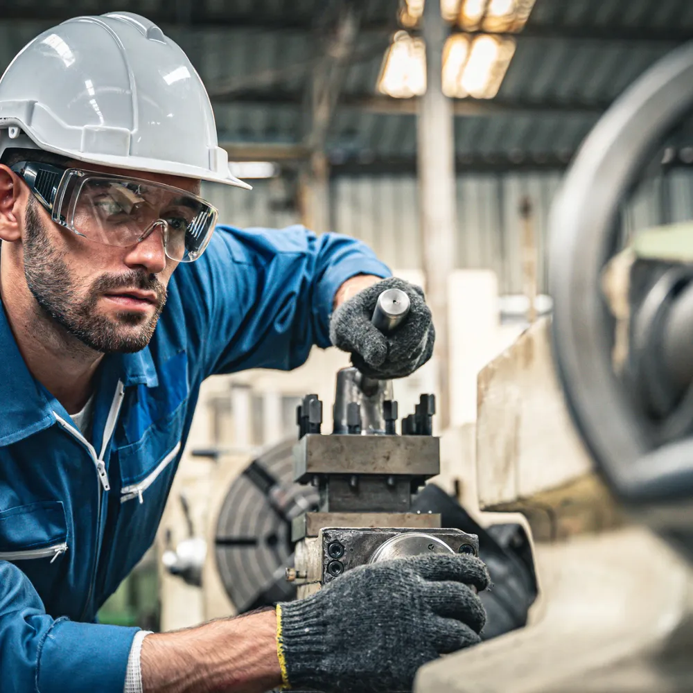 Machinist in safety glasses, helmet and knitted gloves setting up a lathe