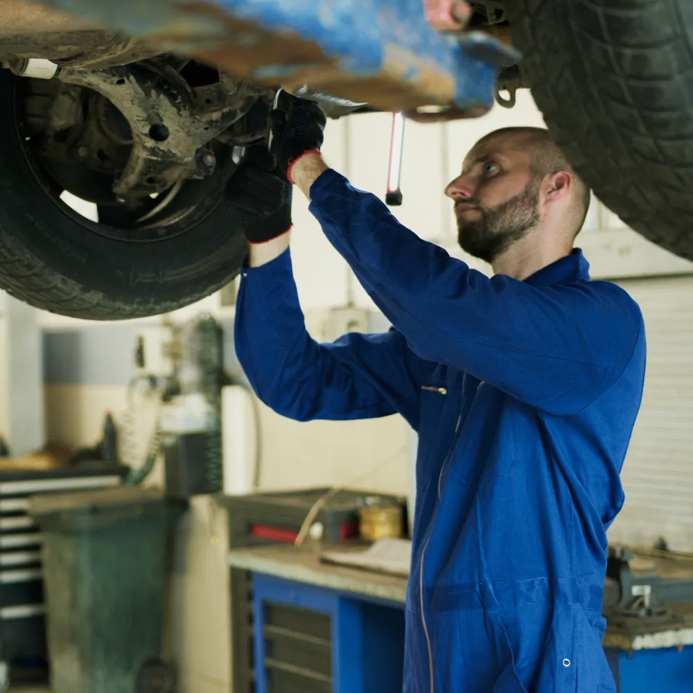 Mechanic in blue coveralls and grip gloves working under a car on a lift