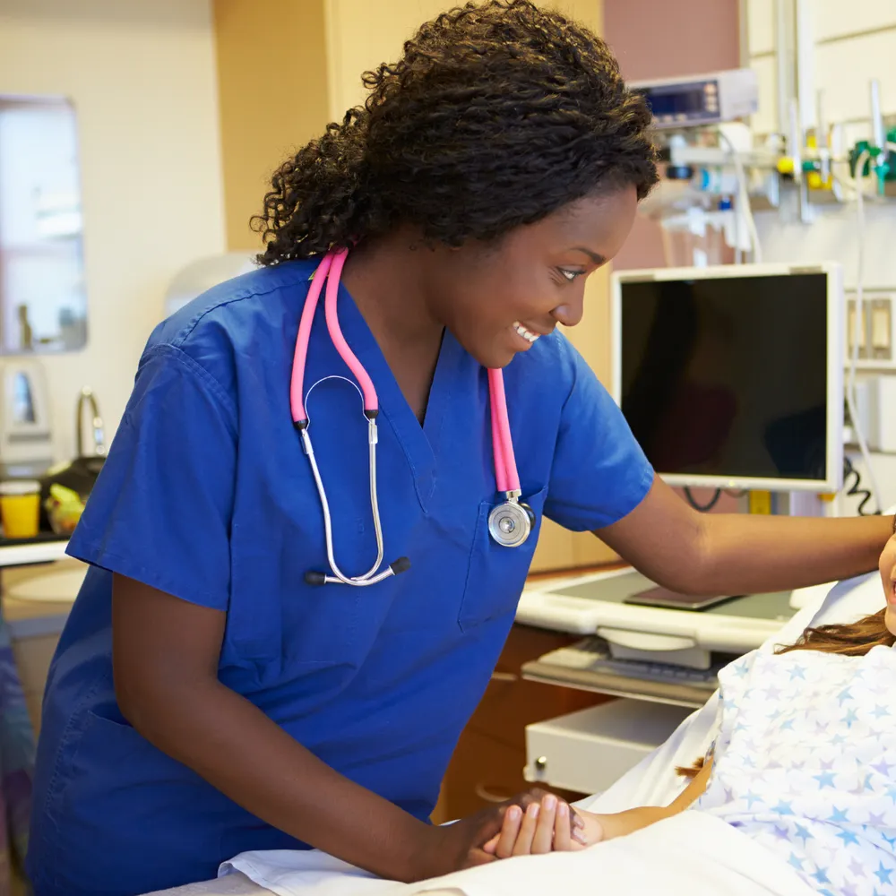 Nurse in blue scrubs with a stethoscope talking to a patient on a ward