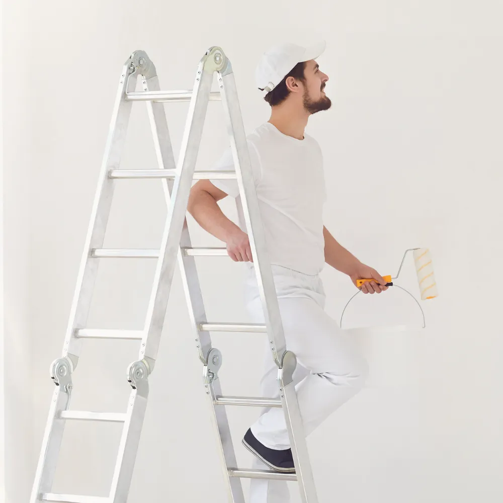 Painter and decorator in whites on a ladder holding a roller and paint kettle