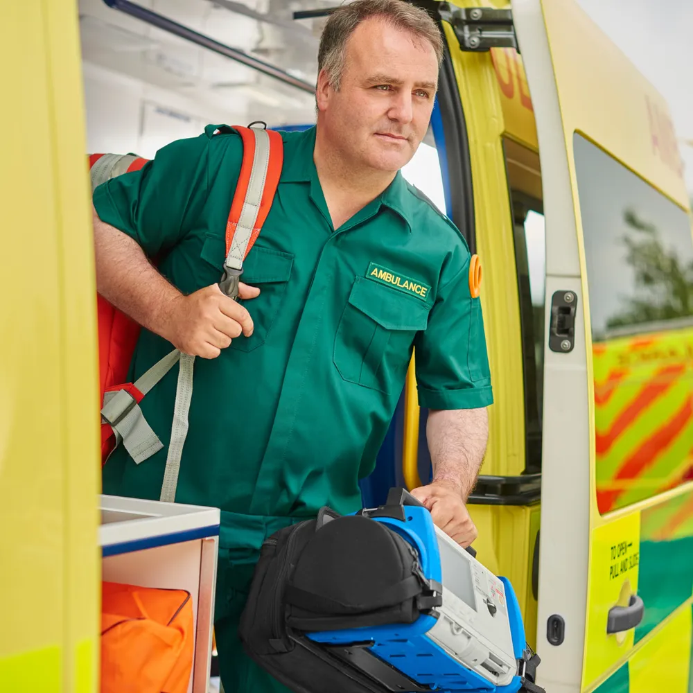 Paramedic in a green uniform unloading kit from the back of an ambulance