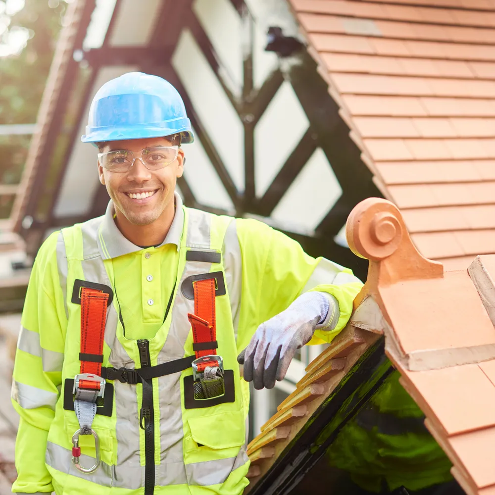Roofer in hi-vis and a safety harness beside a tiled roof ridge
