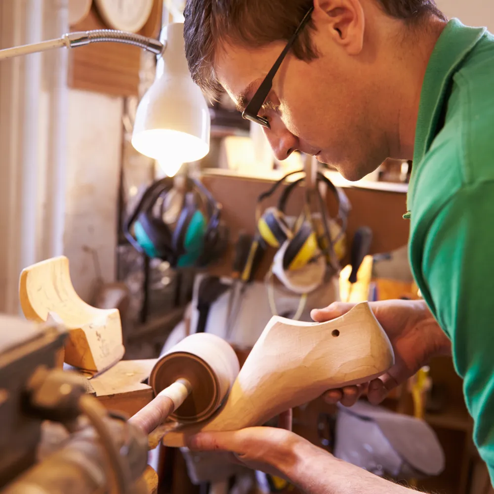 Shoemaker shaping a wooden last at the bench