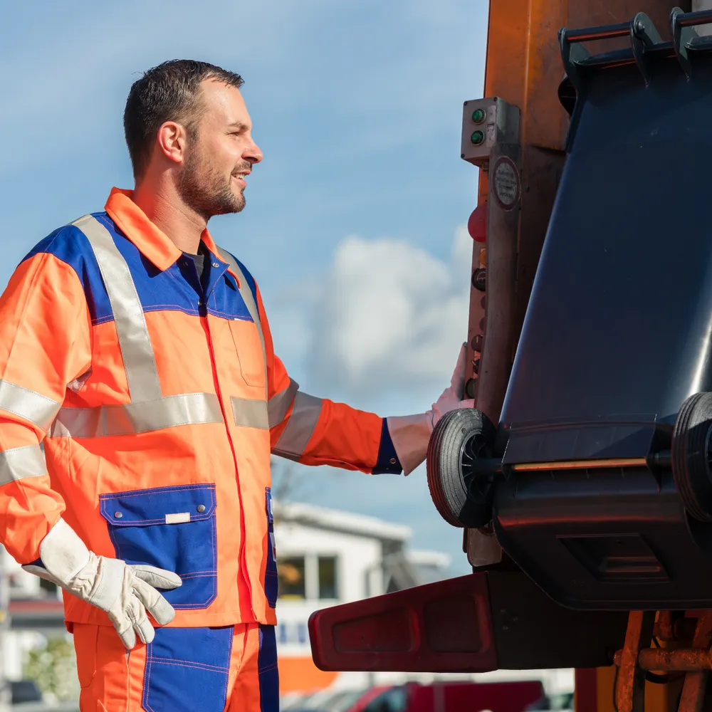 Refuse collector in orange hi-vis loading a wheelie bin onto a refuse truck