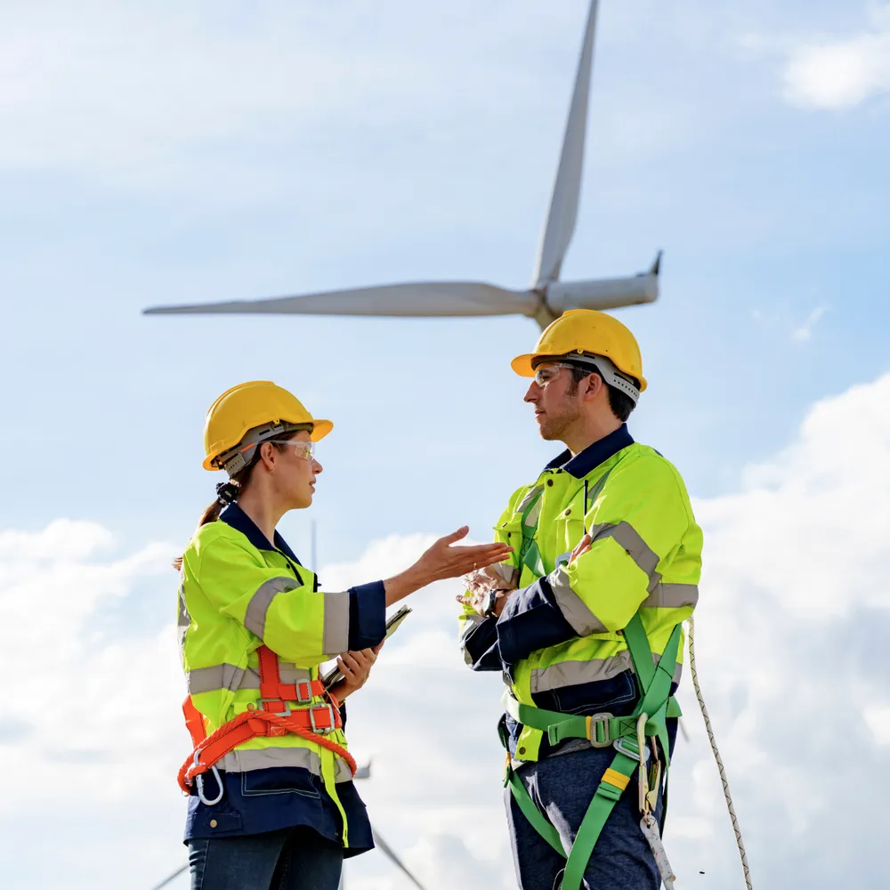 Wind farm technicians in hi-vis and harnesses below a turbine